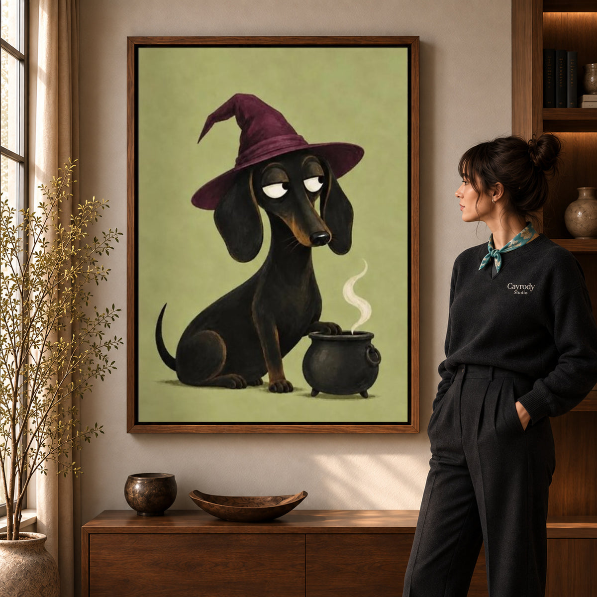 Dachshund Witch canvas art in a walnut frame beside a standing woman and wooden console.
