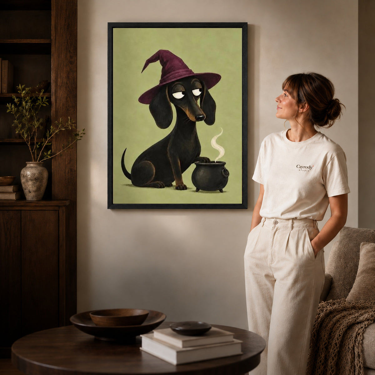 Dachshund Witch canvas art in a black frame above books in a welcoming living room.