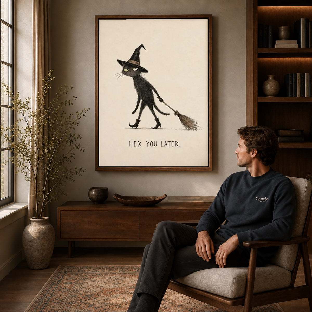 Broomstick Cat canvas art above a wooden console beside a seated man in a warm room.