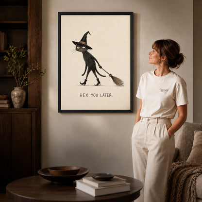 Black framed broomstick cat canvas art displayed beside a woman in a warm living room.