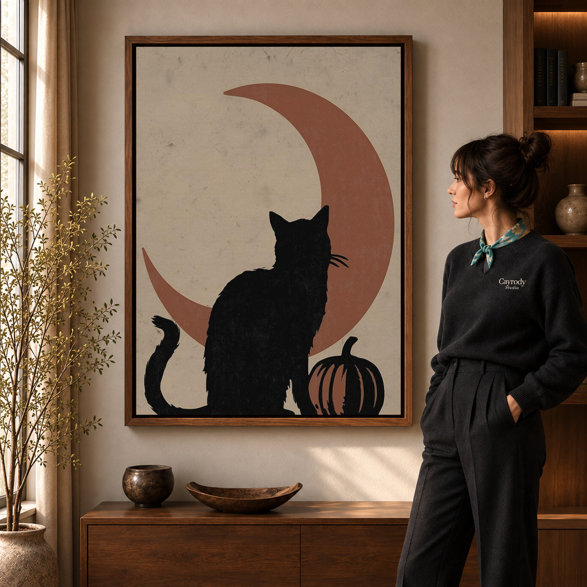 Black Cat Moon canvas art in a walnut frame beside a standing woman and wooden console.
