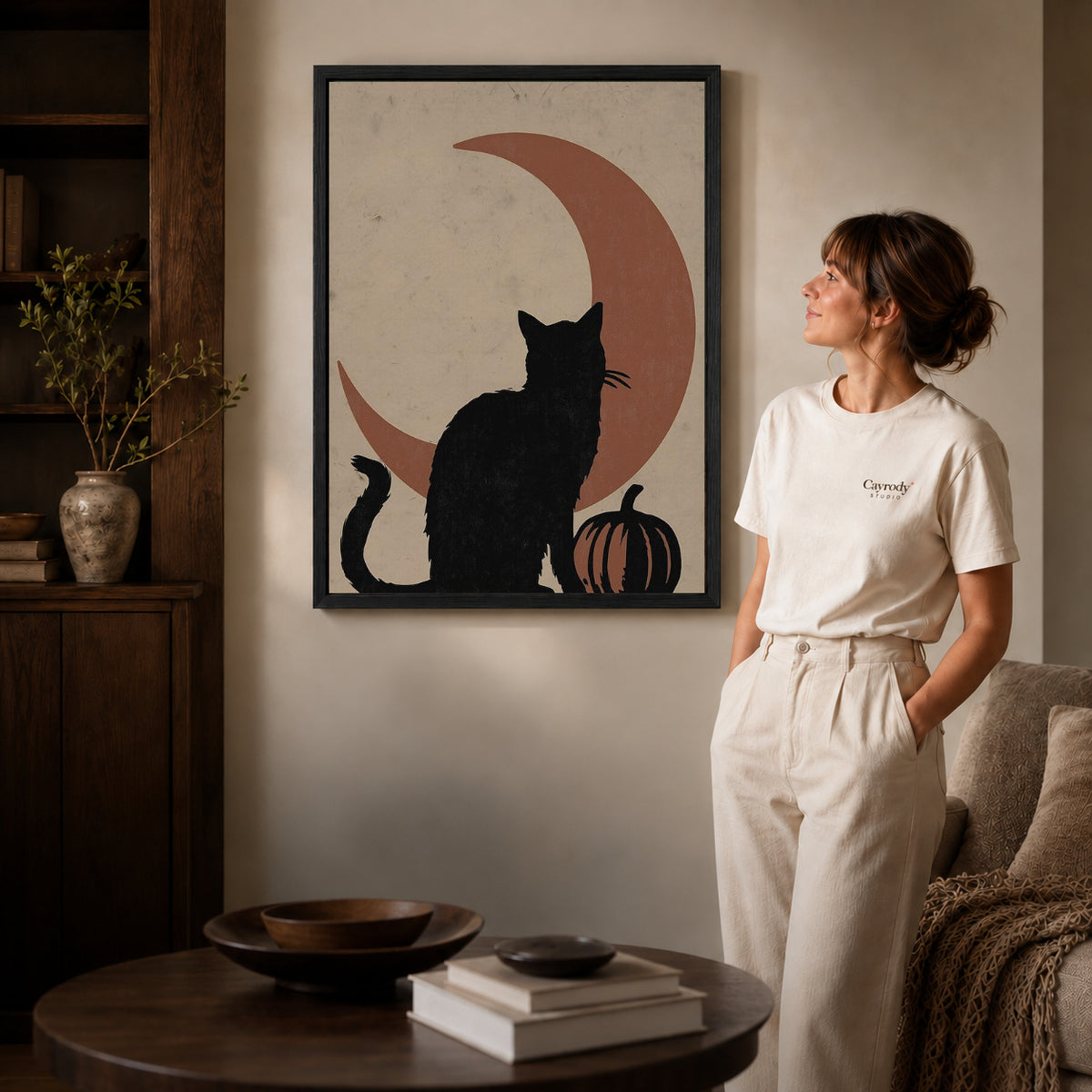 Black framed black cat moon canvas art displayed beside a woman in a warm living room.
