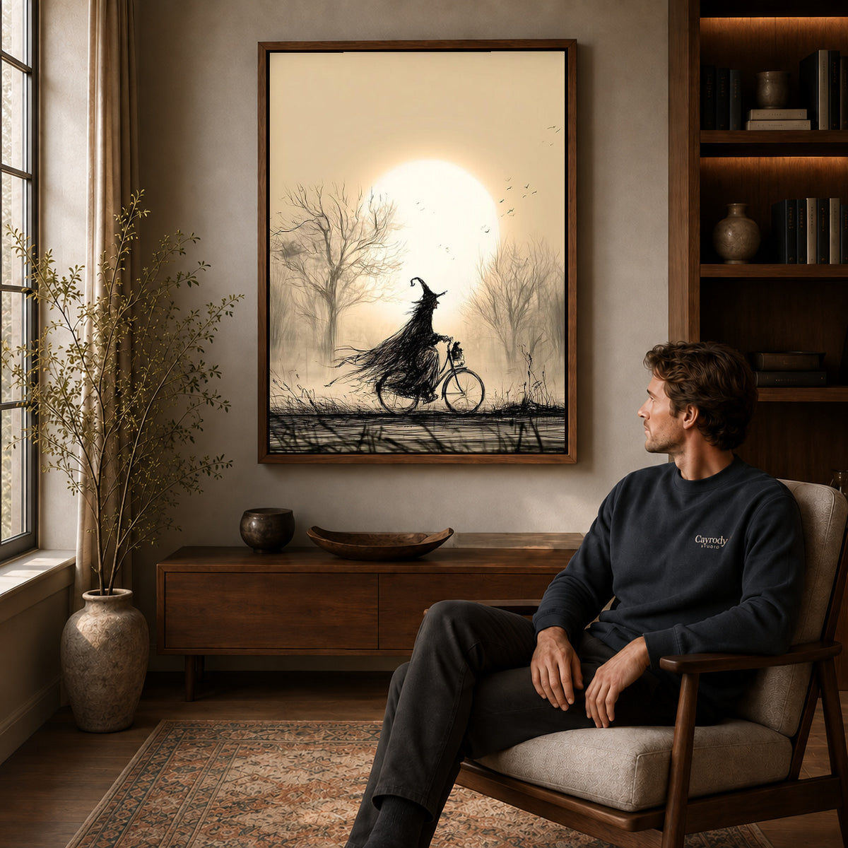 Cycling Witch canvas art above a wooden console beside a seated man in a warm room.