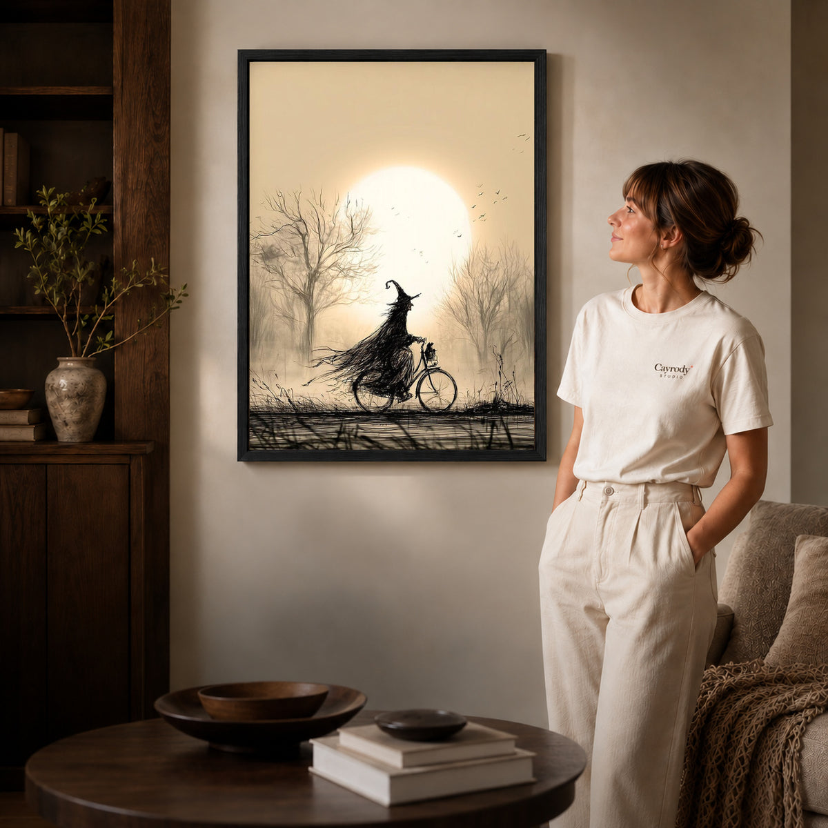 Black framed cycling witch canvas art displayed beside a woman in a warm living room.