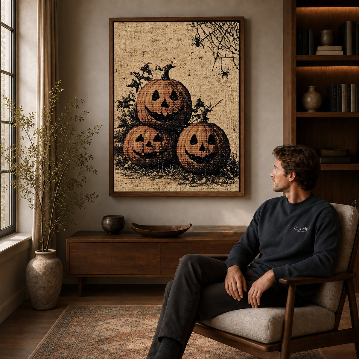 Pumpkin Face Trio canvas art above a wooden console beside a seated man in a warm room.
