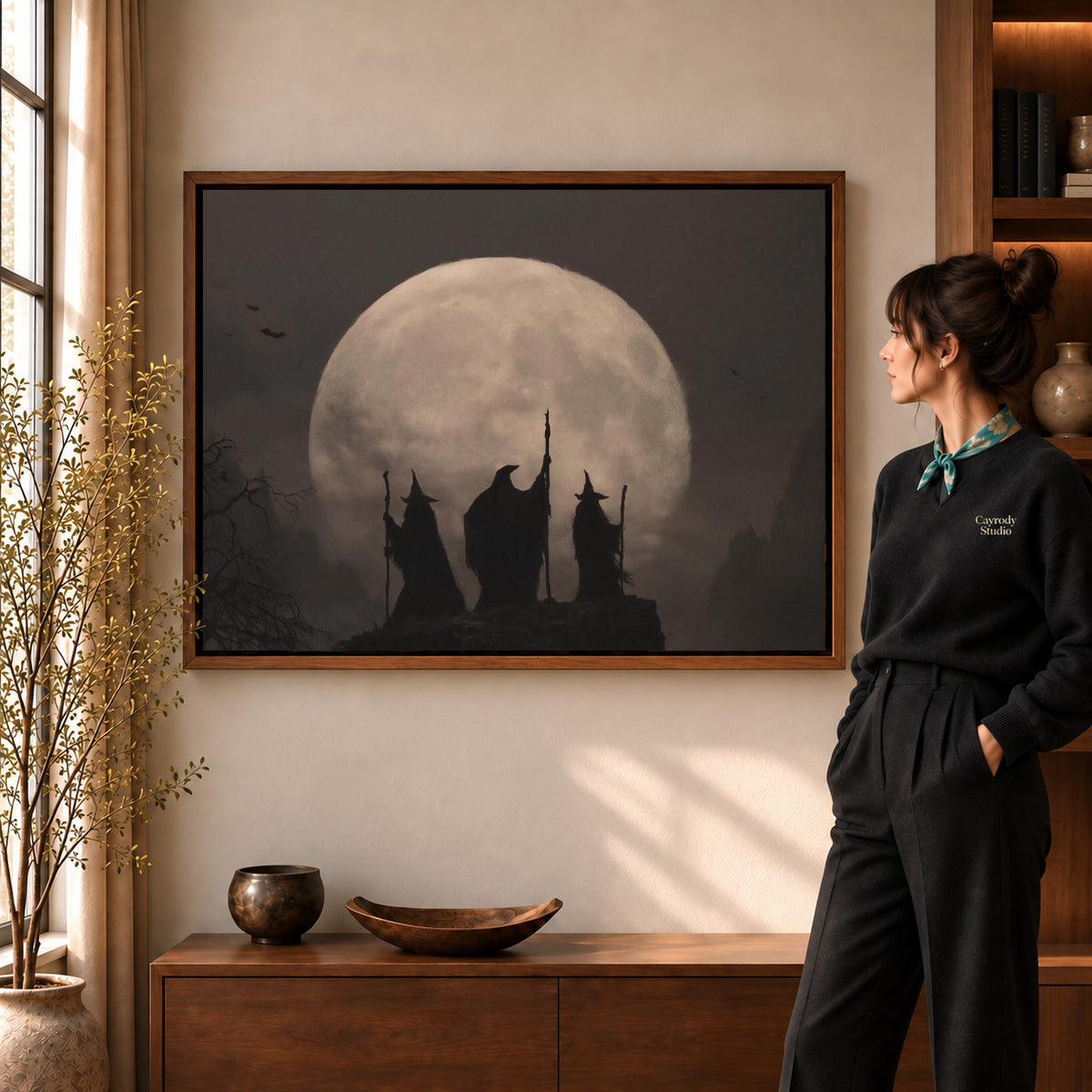 Moonlit Witches canvas art in a walnut frame beside a standing woman and wooden console.
