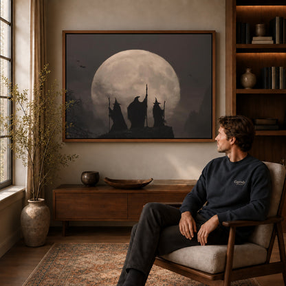Moonlit Witches canvas art above a wooden console beside a seated man in a warm room.