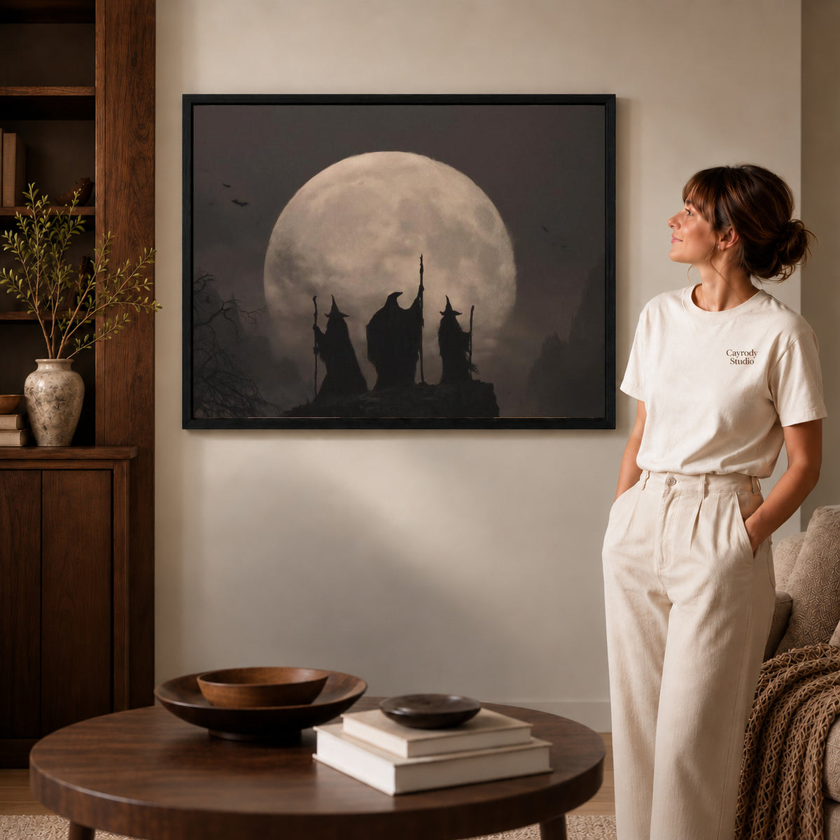 Moonlit Witches canvas art in a black frame above books in a welcoming living room.