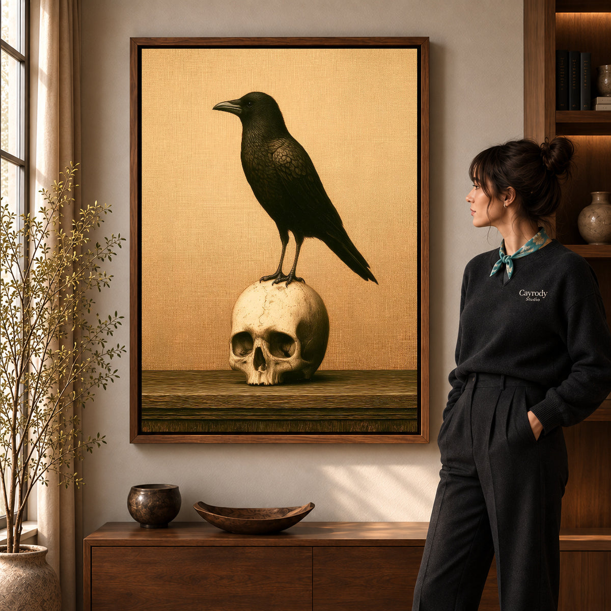 Walnut framed raven and skull canvas art shown beside a standing woman and a wooden console.