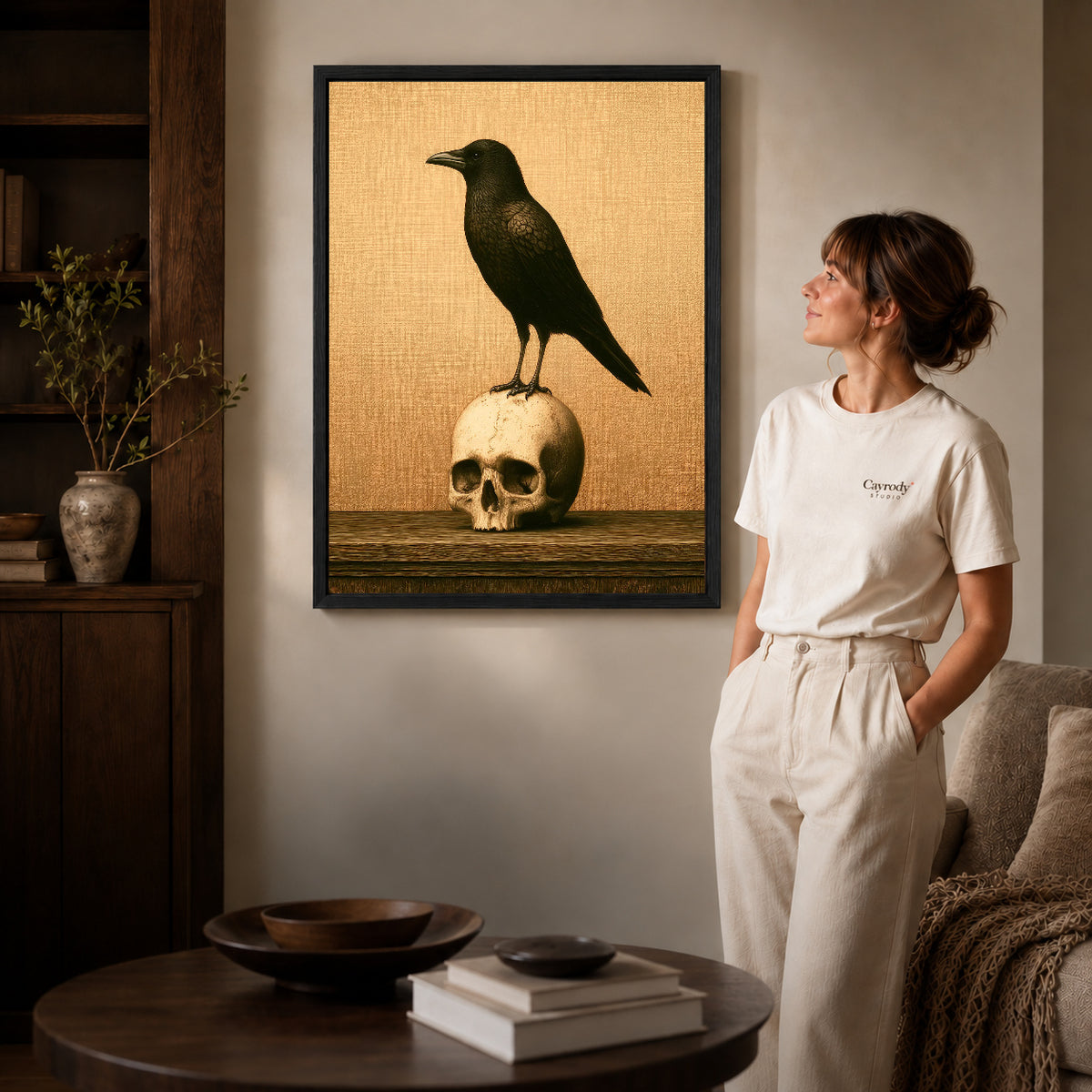 Black framed raven and skull canvas art displayed beside a woman in a warm living room.