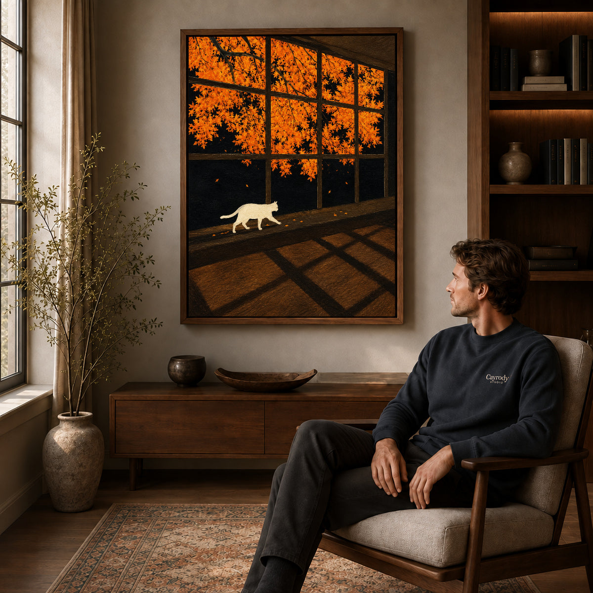 Autumn Window Cat canvas art above a wooden console beside a seated man in a warm room.