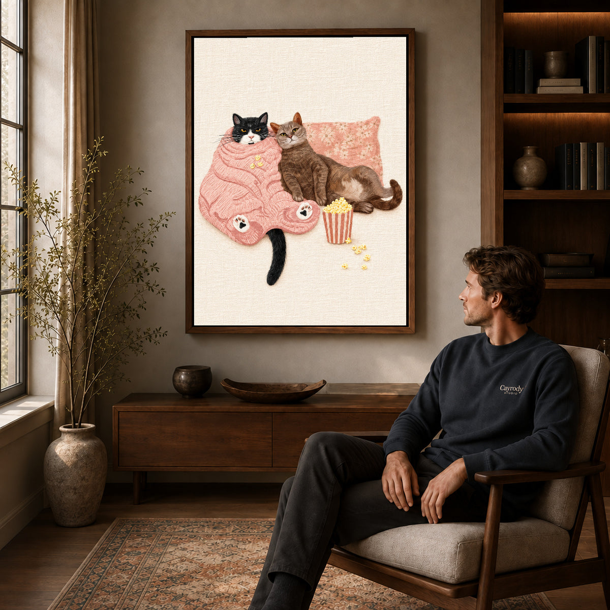 Cozy Movie Cats canvas art above a wooden console beside a seated man in a warm room.