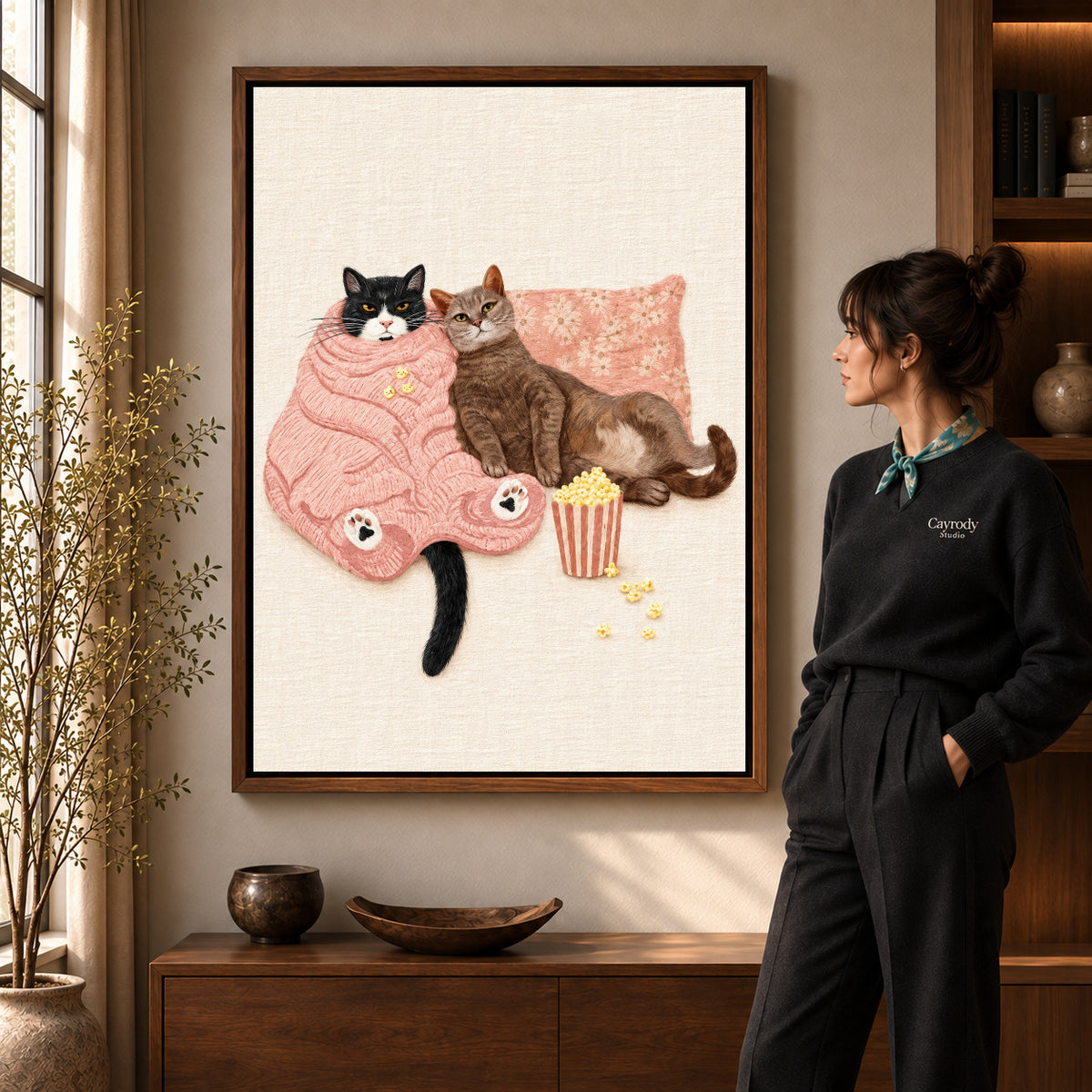 Walnut framed cozy movie cats canvas art shown beside a standing woman and a wooden console.