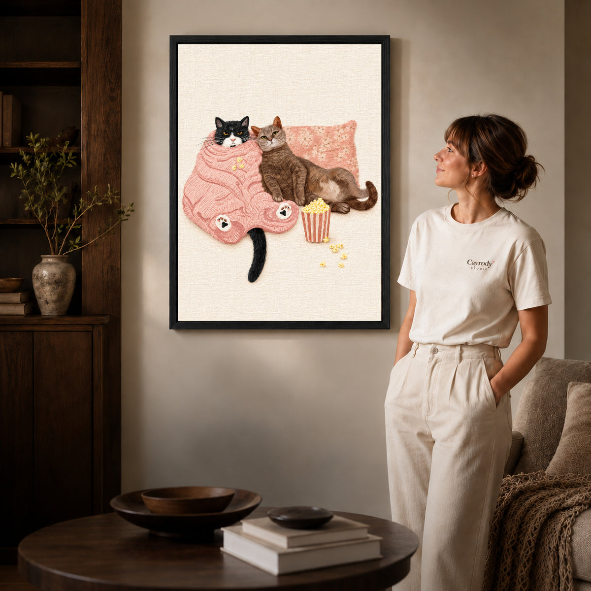 Black framed cozy movie cats canvas art displayed beside a woman in a warm living room.