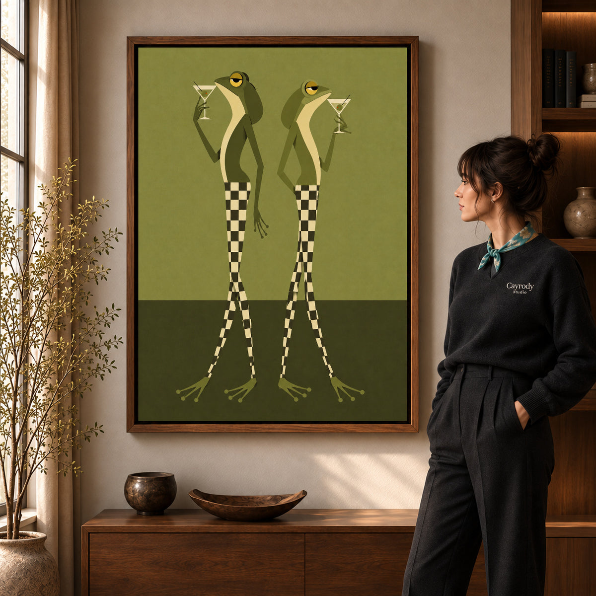 Martini Frogs canvas art in a walnut frame beside a standing woman and wooden console.
