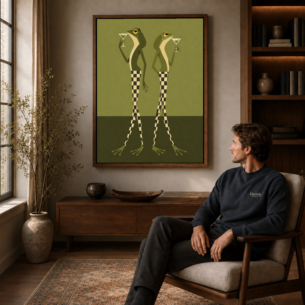Martini Frogs canvas art above a wooden console beside a seated man in a warm room.