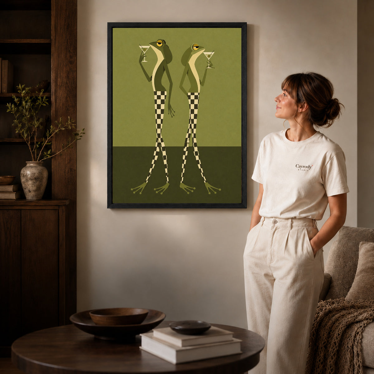 Martini Frogs canvas art in a black frame above books in a welcoming living room.