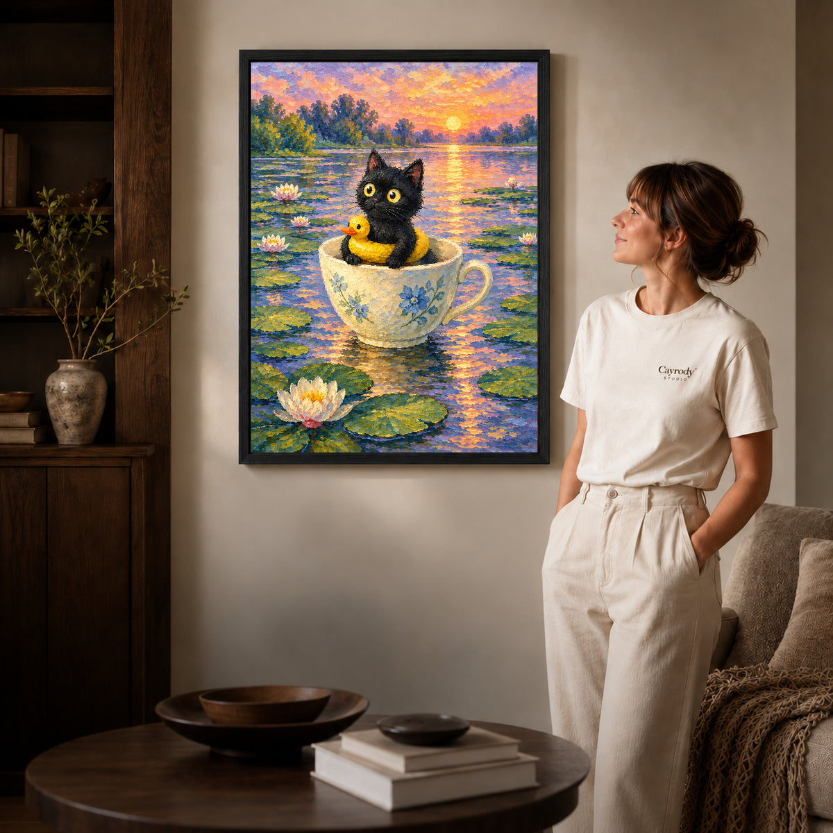 Black framed teacup pond kitten canvas art displayed beside a woman in a warm living room.