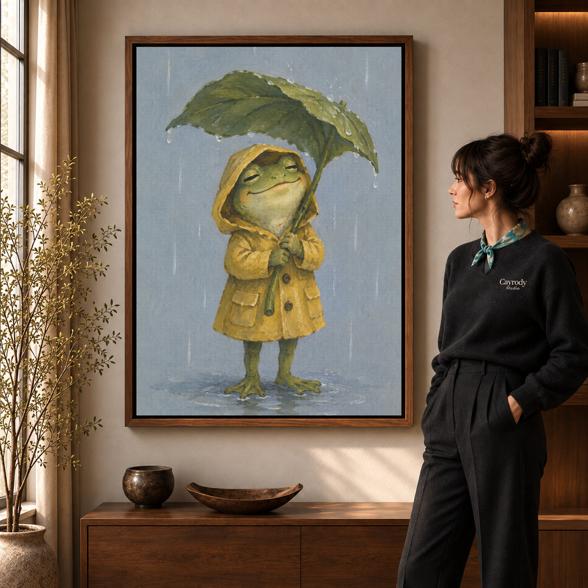 Walnut framed raincoat frog canvas art shown beside a standing woman and a wooden console.