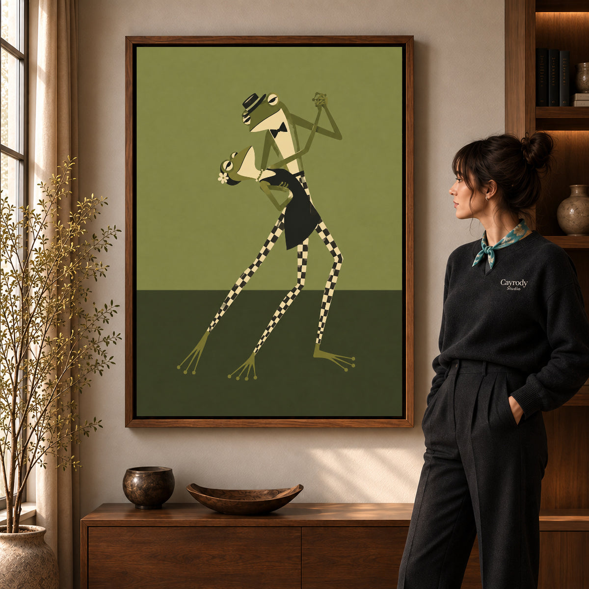 Walnut framed dancing frogs canvas art shown beside a standing woman and a wooden console.