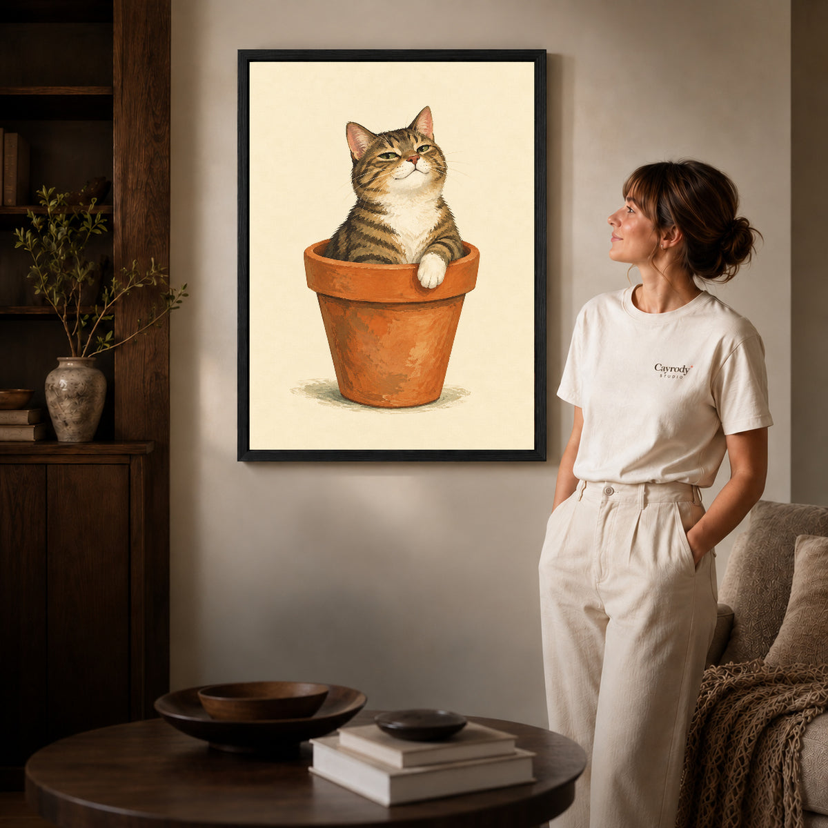 Black framed flowerpot cat canvas art displayed beside a woman in a warm living room.