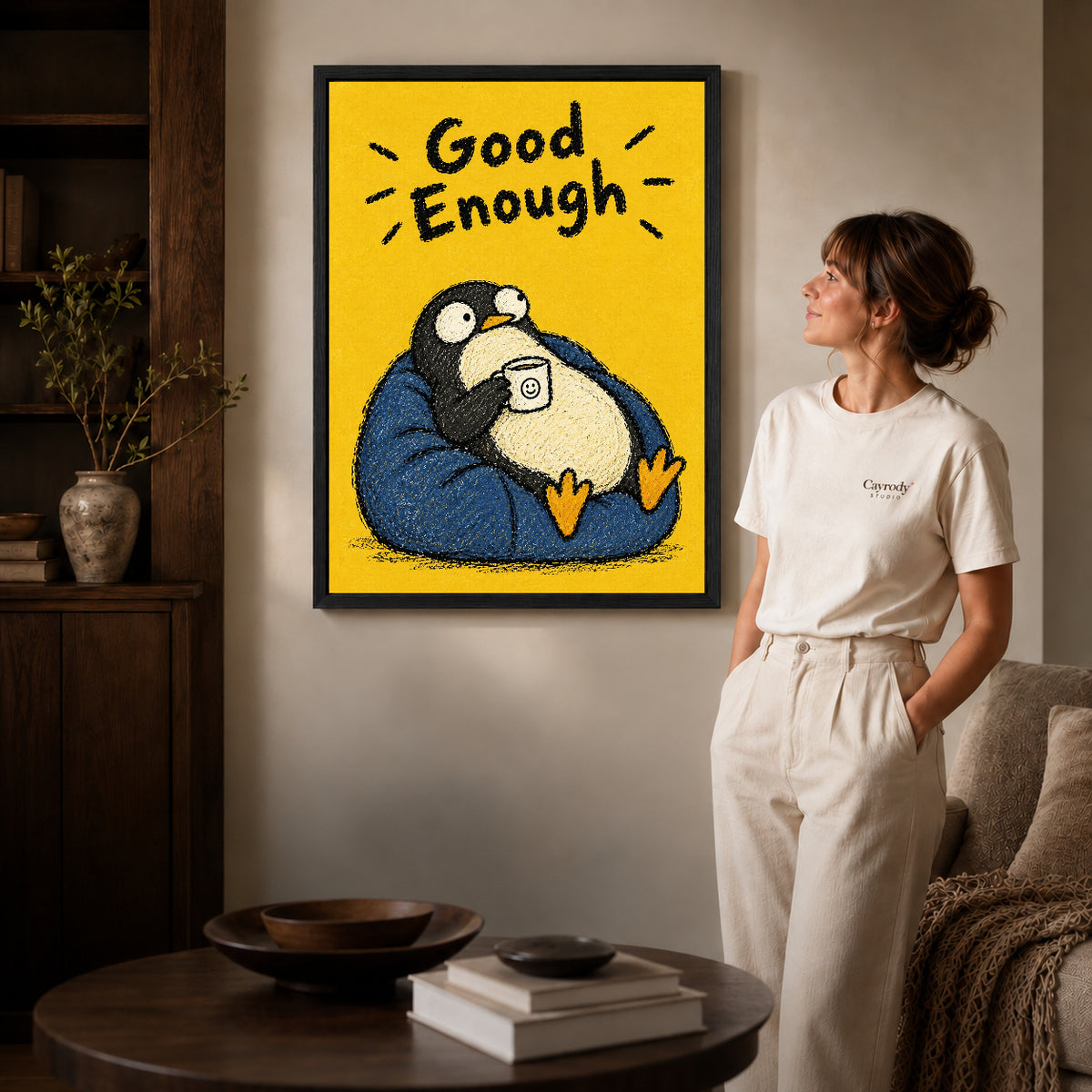 Black framed resting penguin canvas art displayed beside a woman in a warm living room.