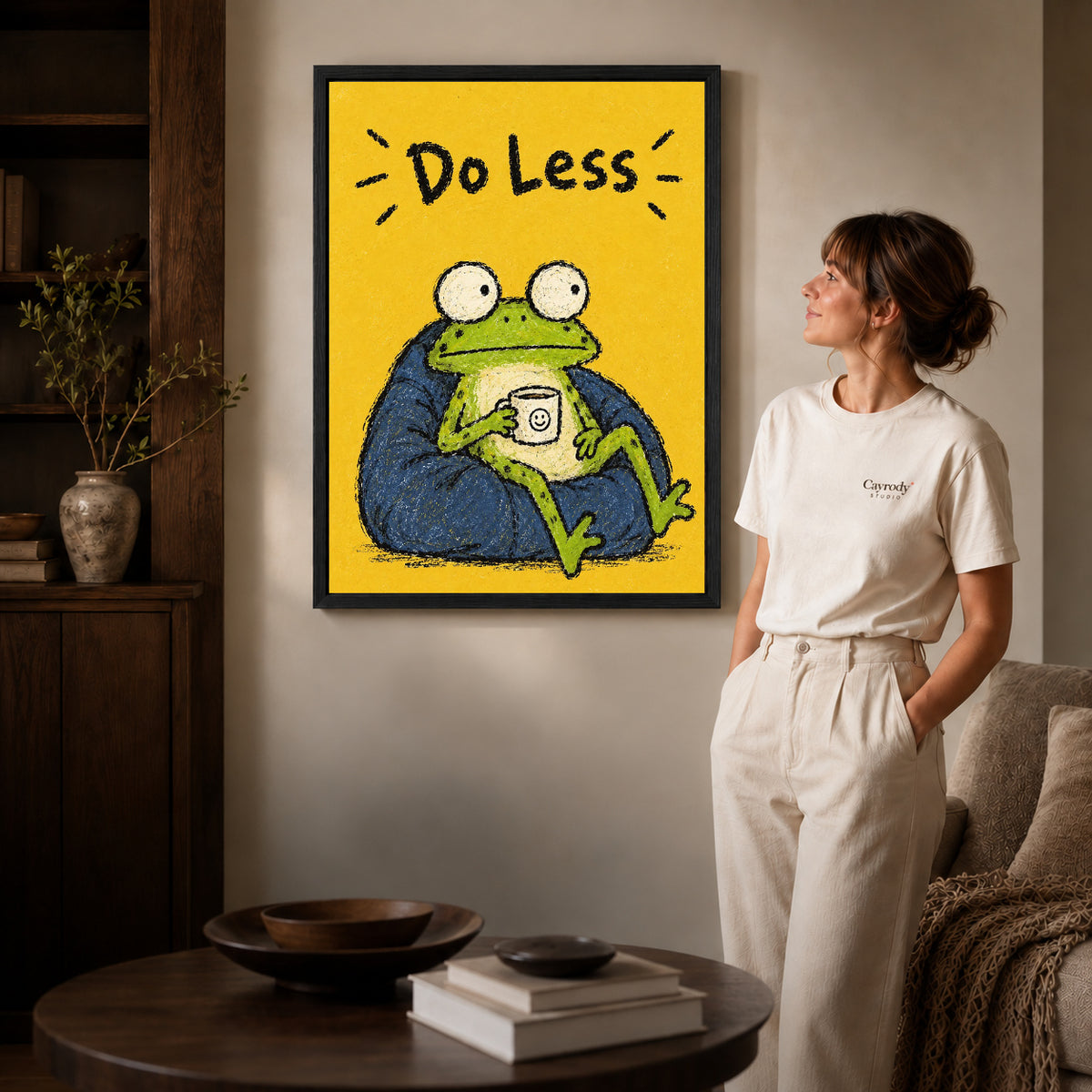 Black framed resting frog canvas art displayed beside a woman in a warm living room.