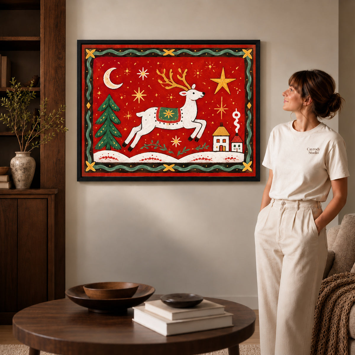 Black framed festive folk reindeer canvas art displayed beside a woman in a warm living room.