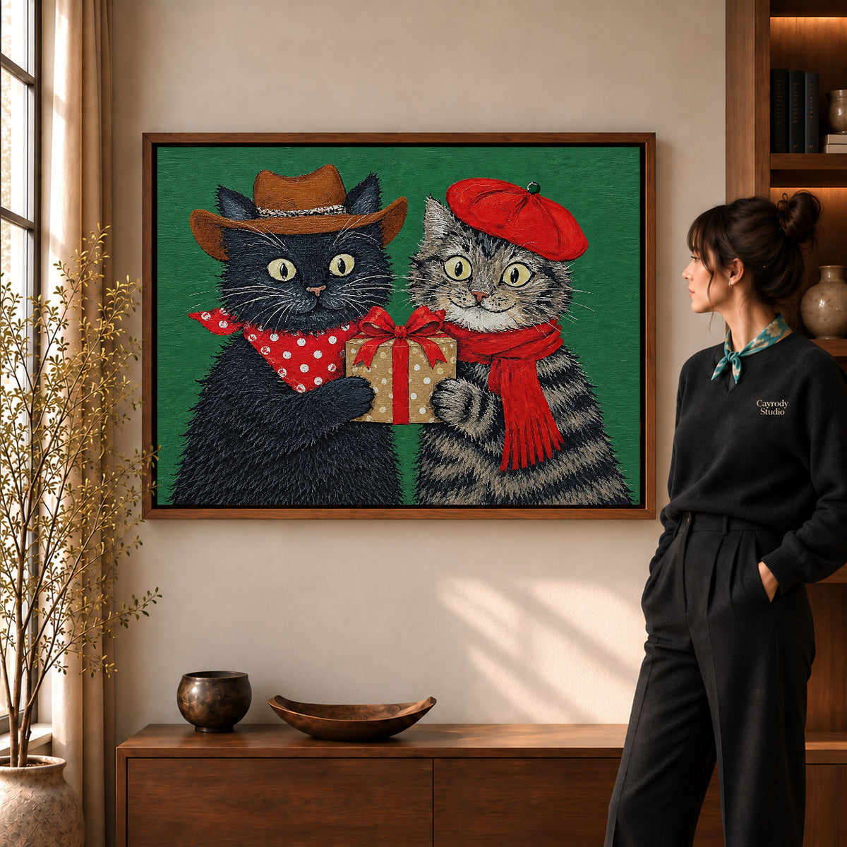 Holiday Gift Cats canvas art in a walnut frame beside a standing woman and wooden console.