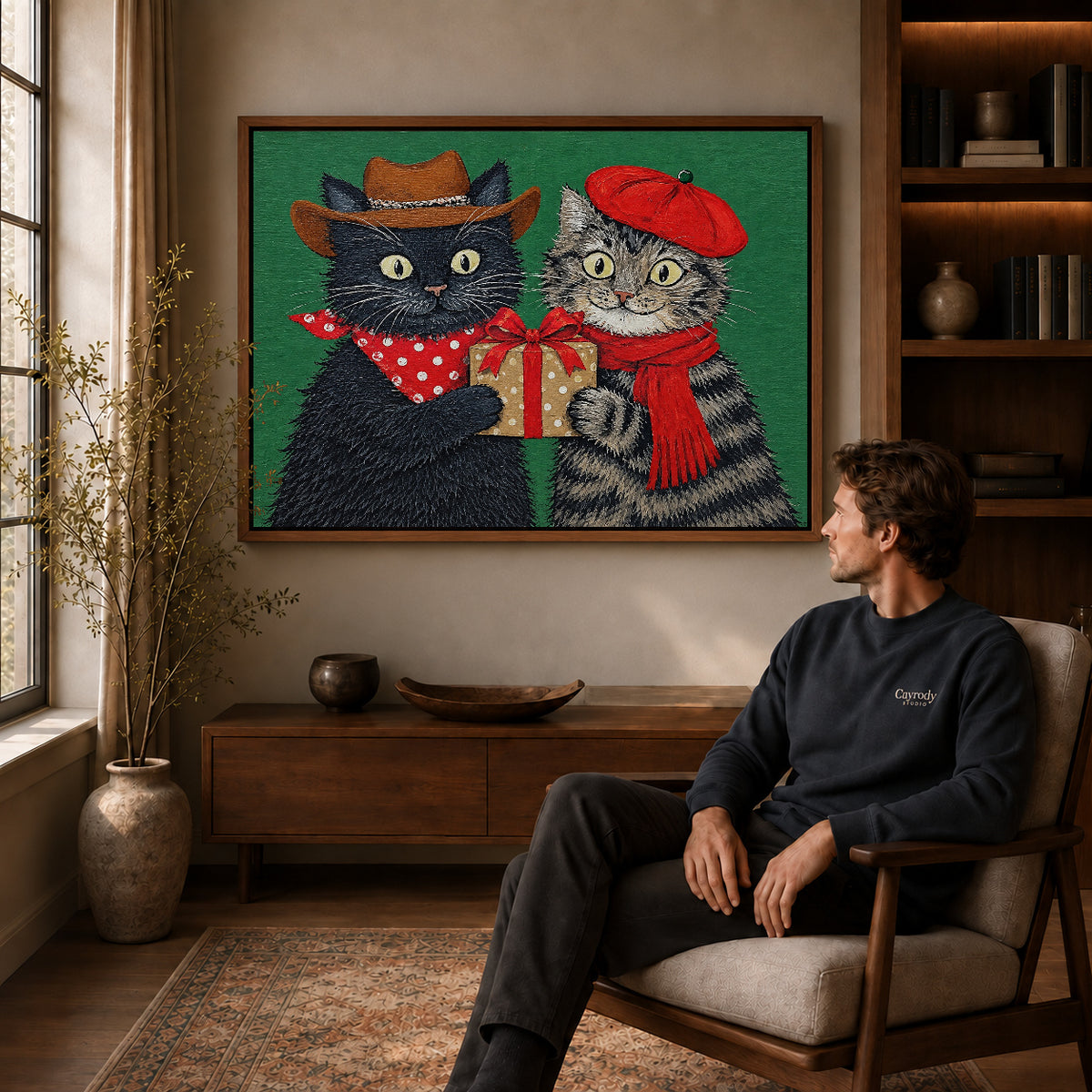 Holiday Gift Cats canvas art above a wooden console beside a seated man in a warm room.