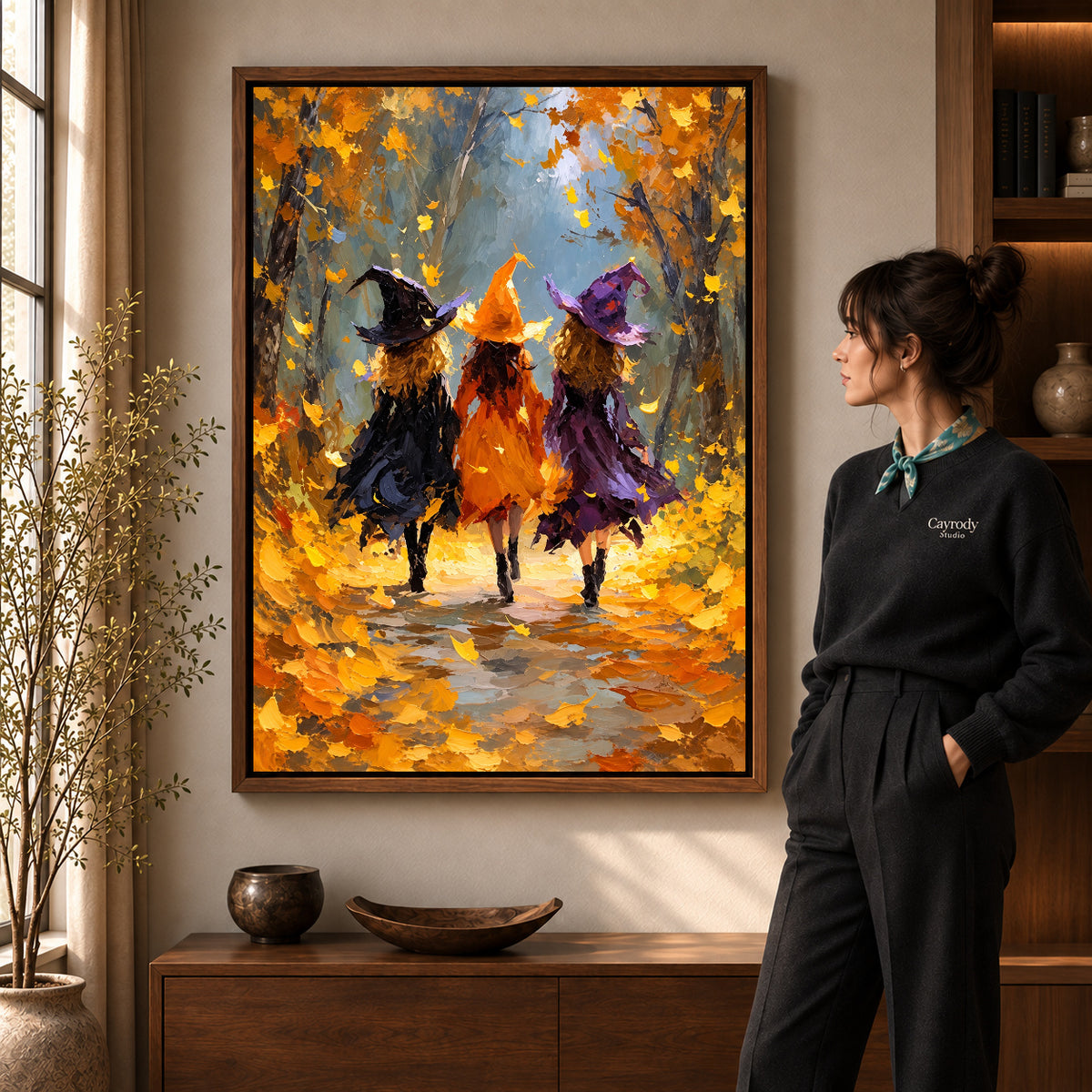 Walnut framed autumn witch friends canvas art shown beside a standing woman and a wooden console.