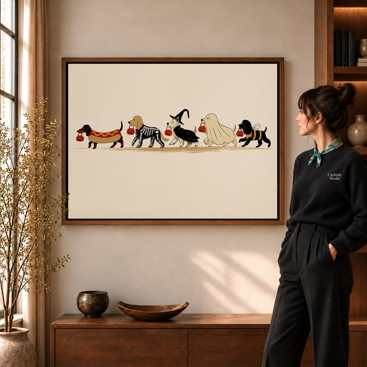 Costumed Dog Parade canvas art in a walnut frame beside a standing woman and wooden console.