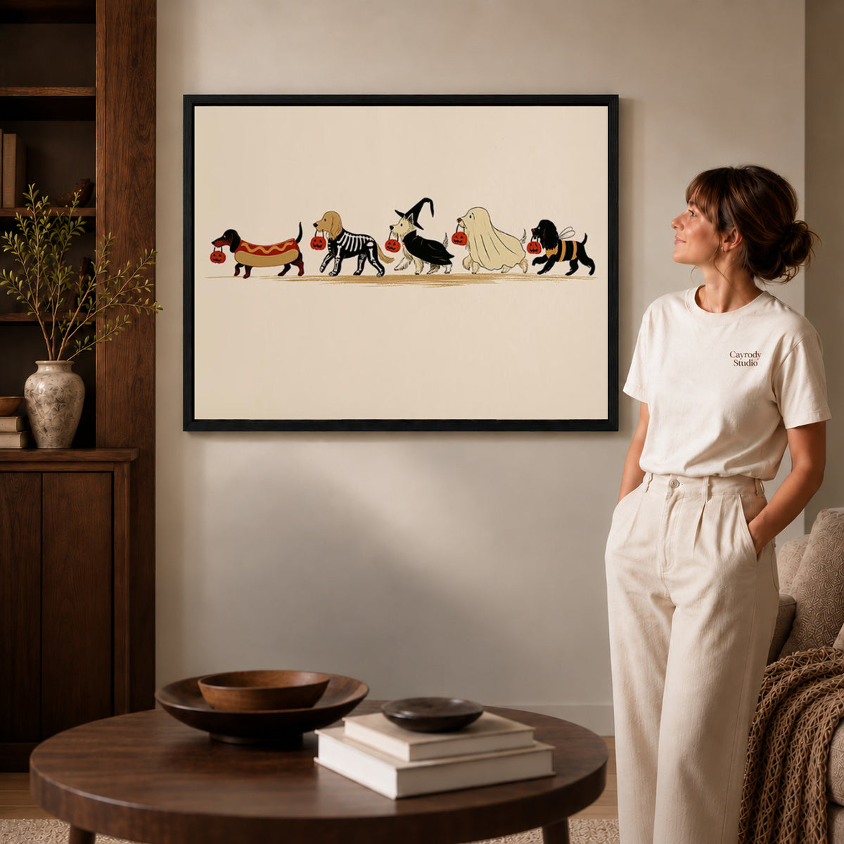 Black framed costumed dog parade canvas art displayed beside a woman in a warm living room.