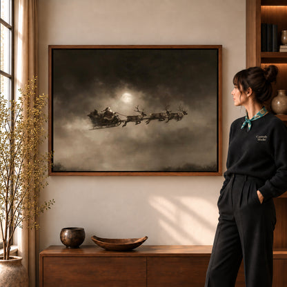 Moonlit Sleigh canvas art in a walnut frame beside a standing woman and wooden console.