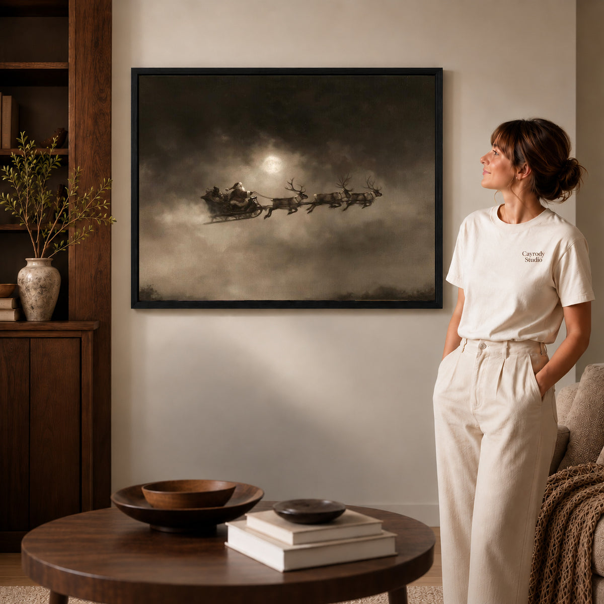 Moonlit Sleigh canvas art in a black frame above books in a welcoming living room.
