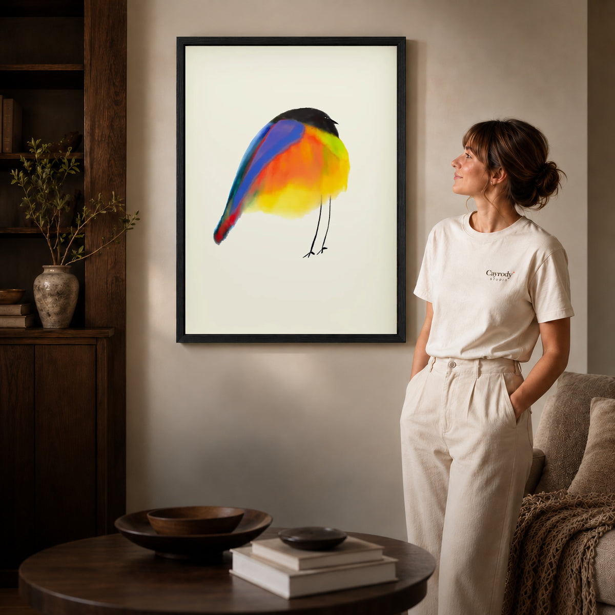 Black framed colorful bird canvas art displayed beside a woman in a warm living room.