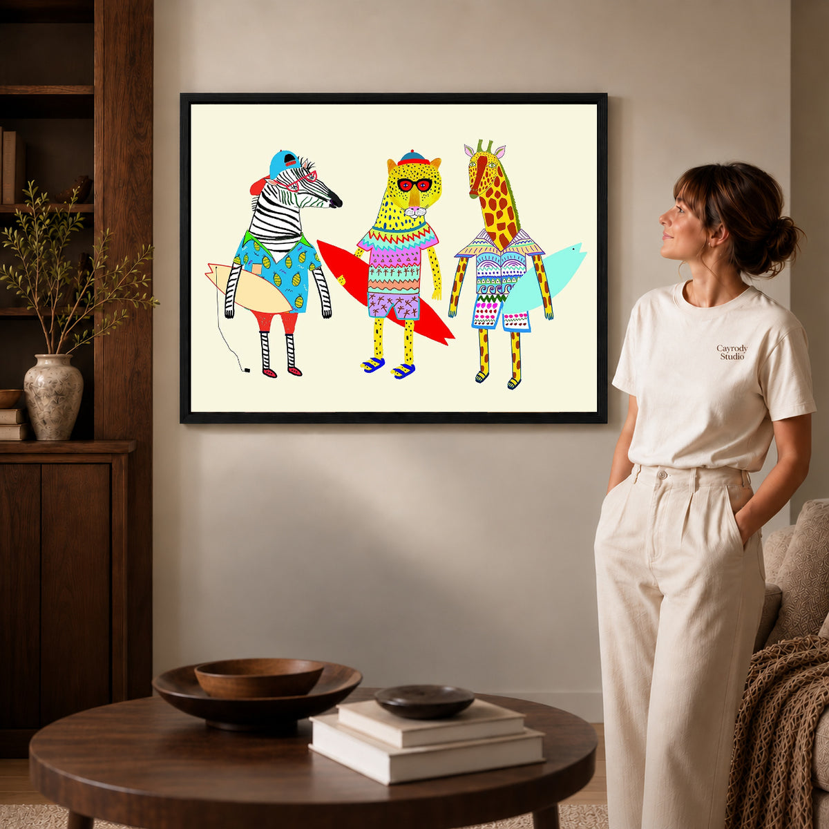 Black framed surfing animals canvas art displayed beside a woman in a warm living room.