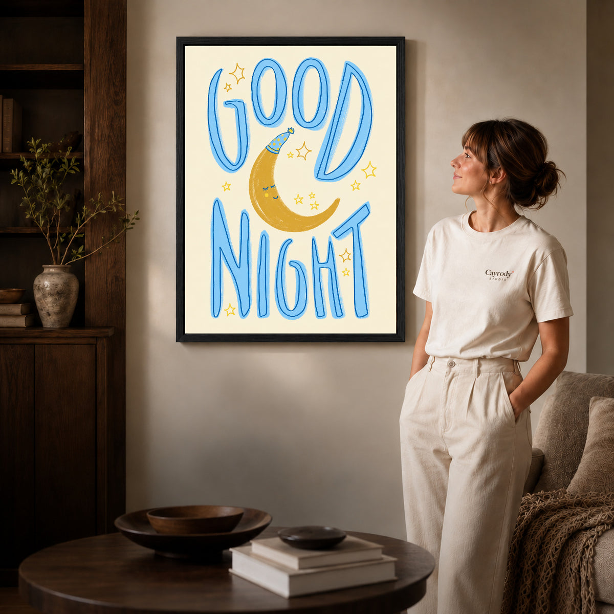 good night moon art canvas art in a black frame beside a woman and round wooden table.