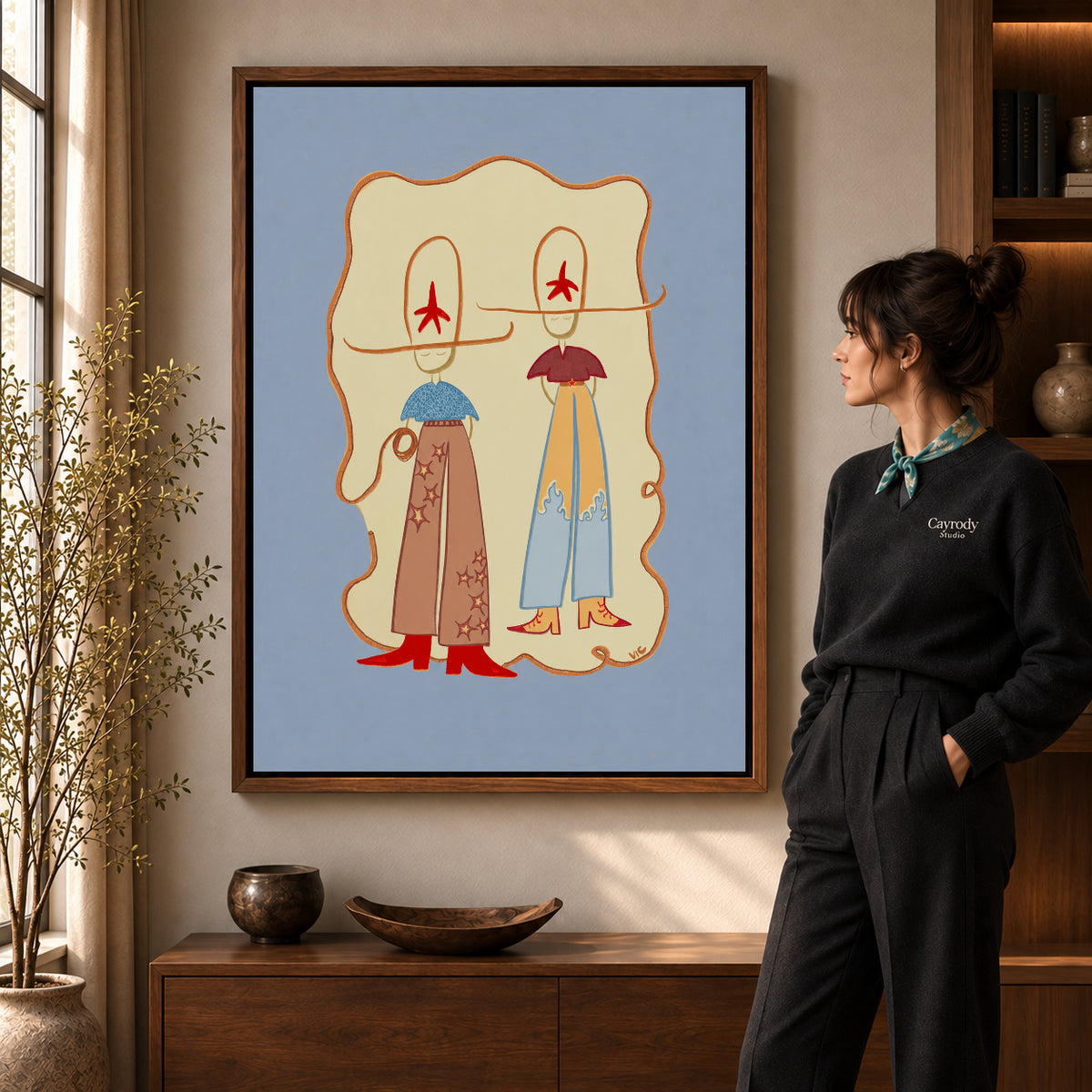 Western Cowgirl Duo canvas art in a walnut frame beside a standing woman and wooden console.
