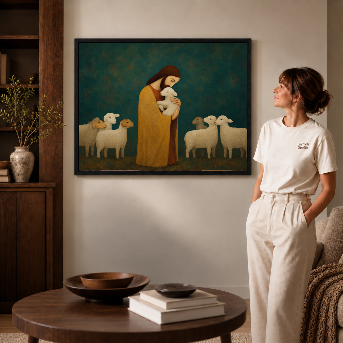 Black framed gentle shepherd canvas art displayed beside a woman in a warm living room.