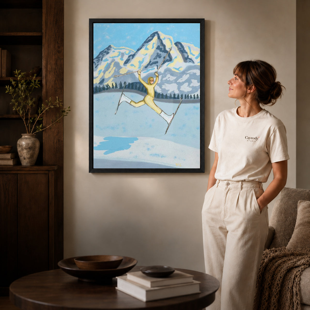 Black framed joyful skier canvas art displayed beside a woman in a warm living room.