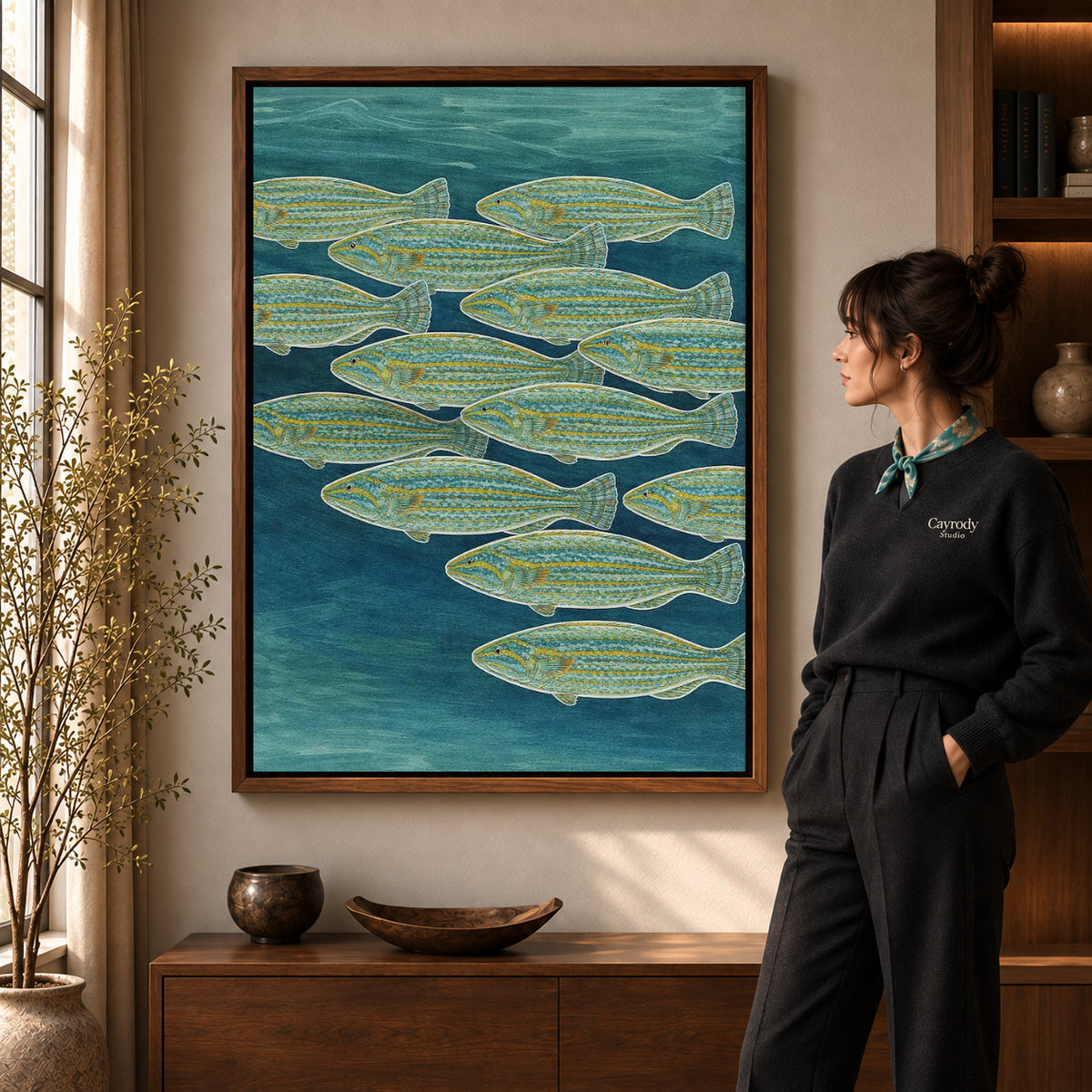 Swimming Fish canvas art in a walnut frame beside a standing woman and wooden console.