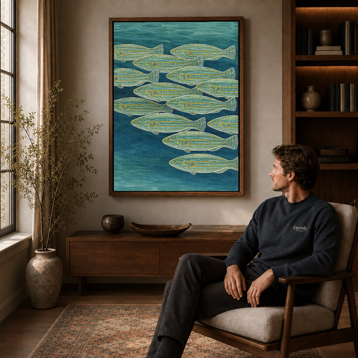 Swimming Fish canvas art above a wooden console beside a seated man in a warm room.