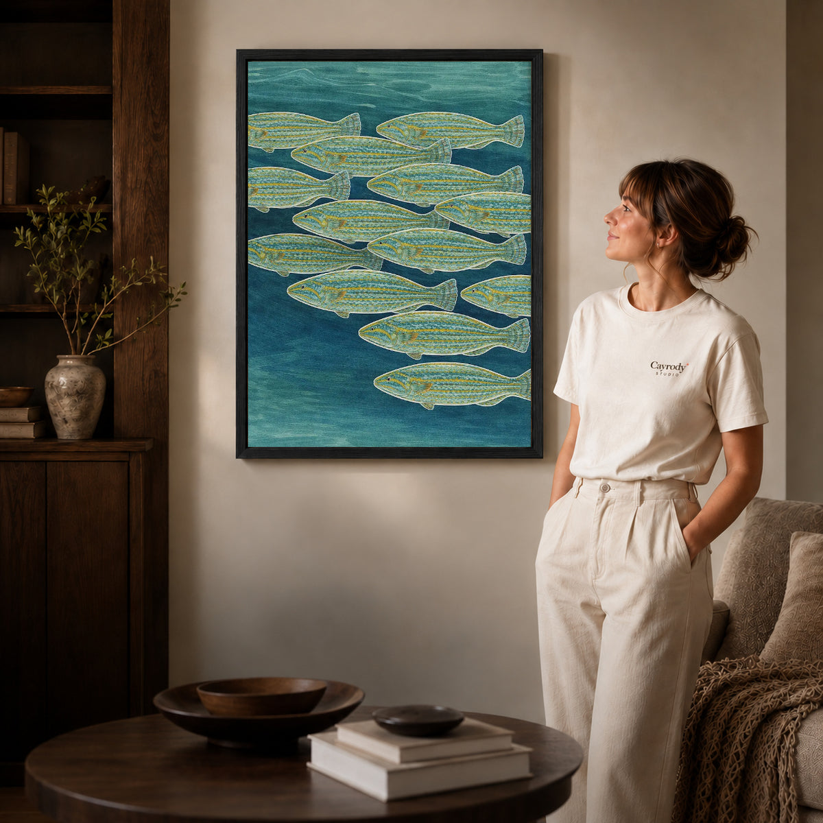 Swimming Fish canvas art in a black frame above books in a welcoming living room.