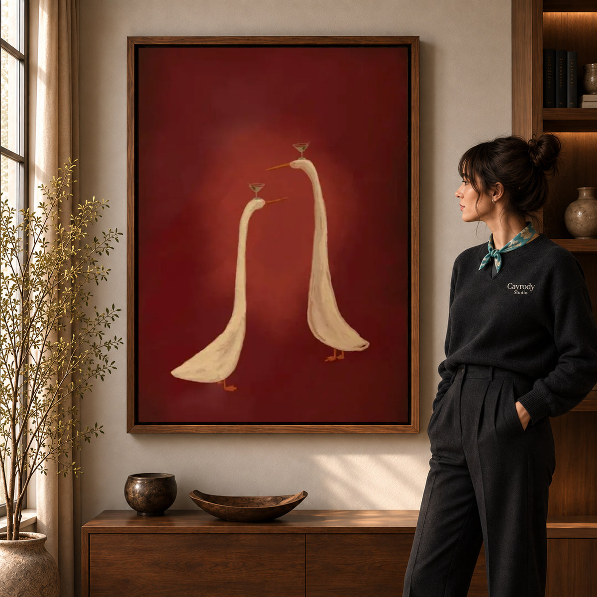 Cocktail Geese canvas art in a walnut frame beside a standing woman and wooden console.