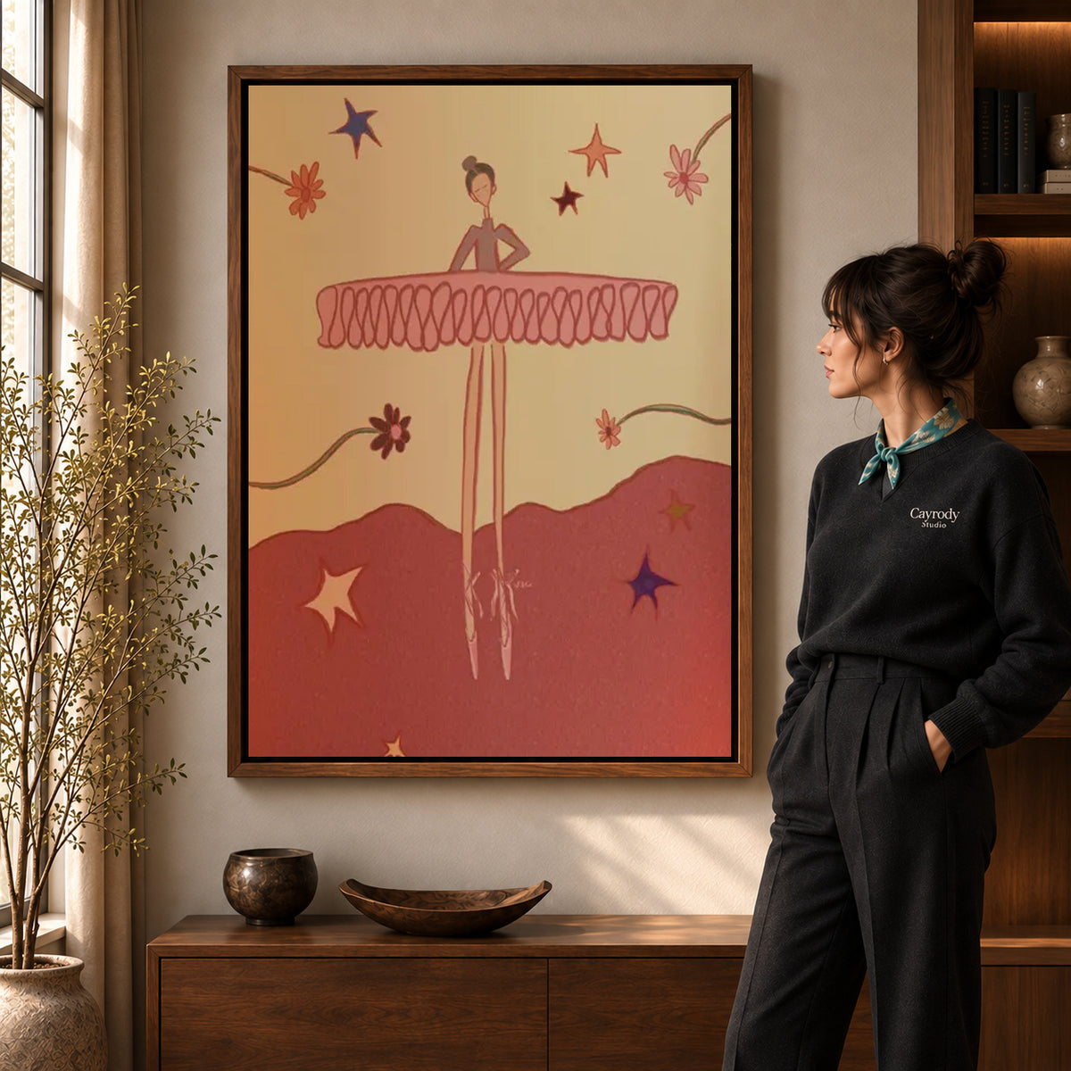 Playful Ballerina canvas art in a walnut frame beside a standing woman and wooden console.
