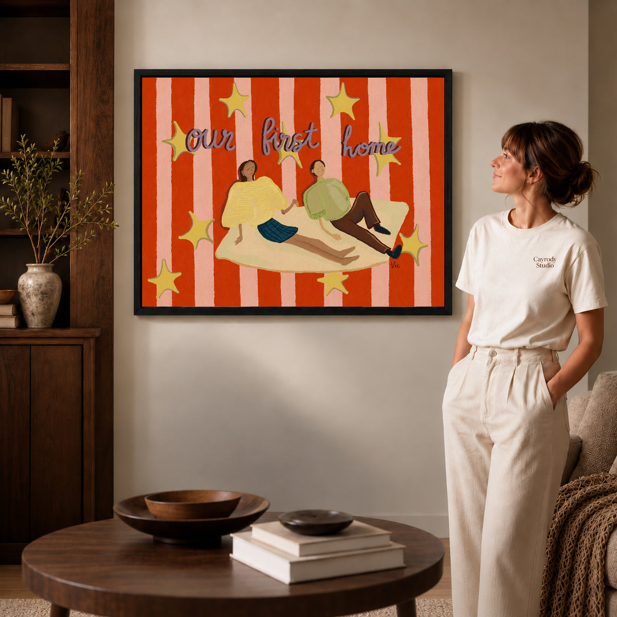 First Home Couple canvas art in a black frame above books in a welcoming living room.