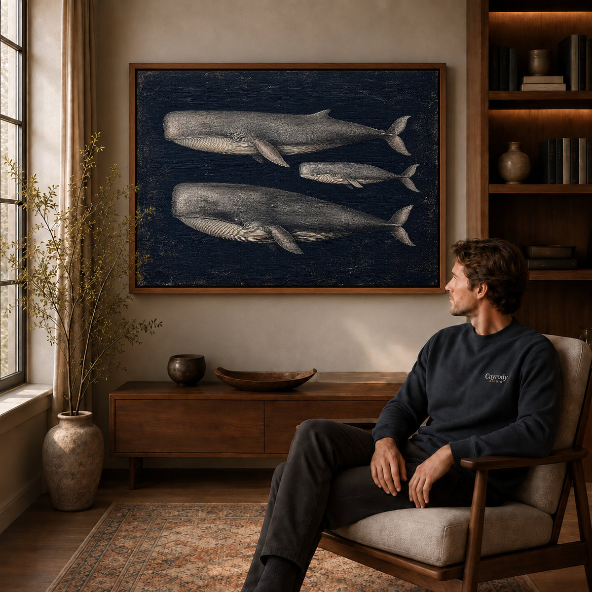Vintage Whale Trio canvas art above a wooden console beside a seated man in a warm room.