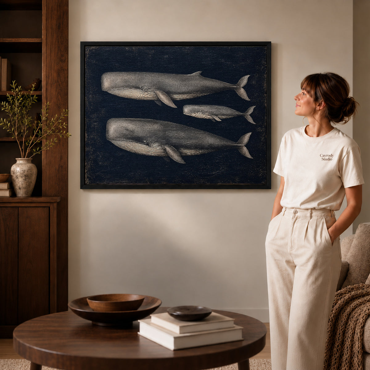 Vintage Whale Trio canvas art in a black frame above books in a welcoming living room.