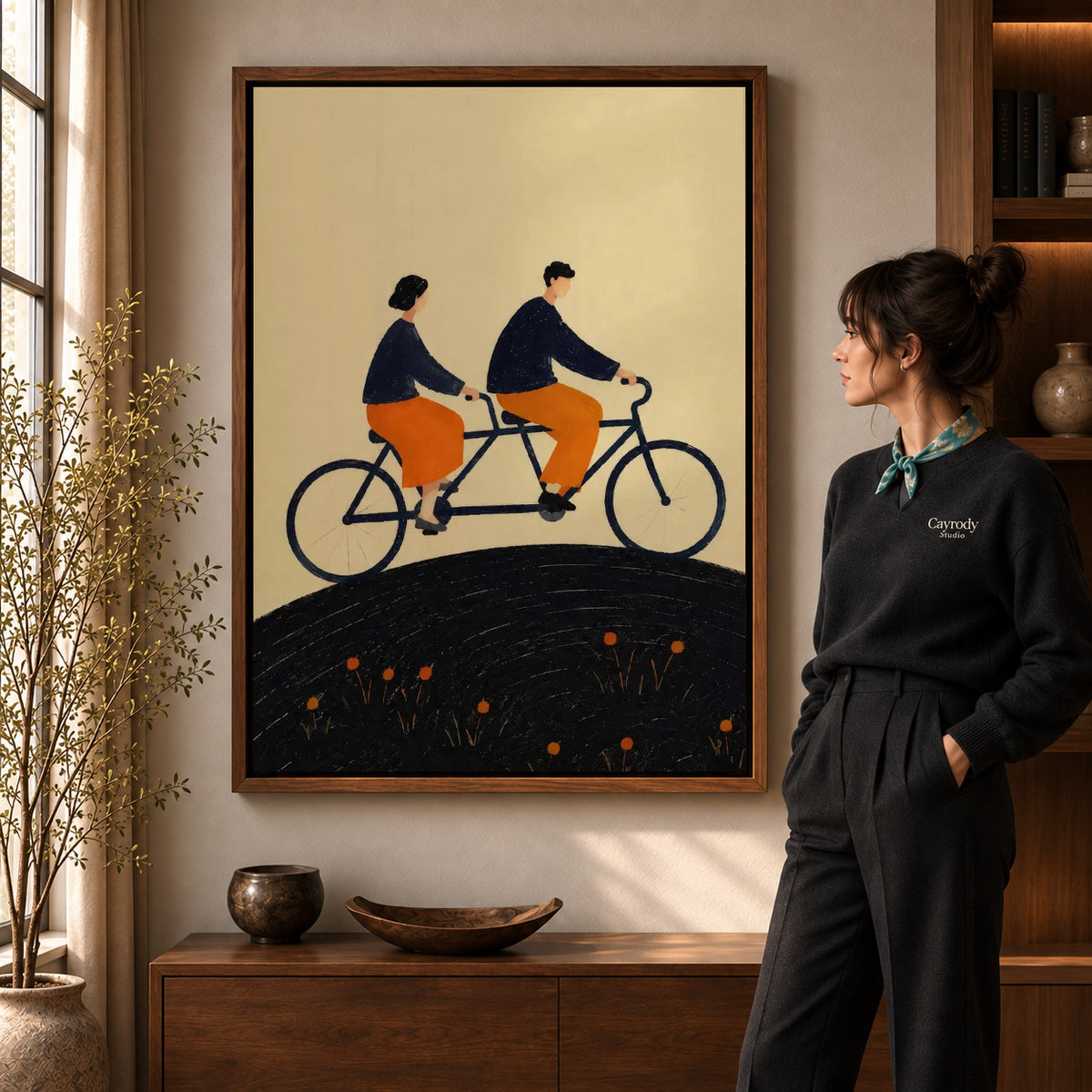 Tandem Ride canvas art in a walnut frame beside a standing woman and wooden console.
